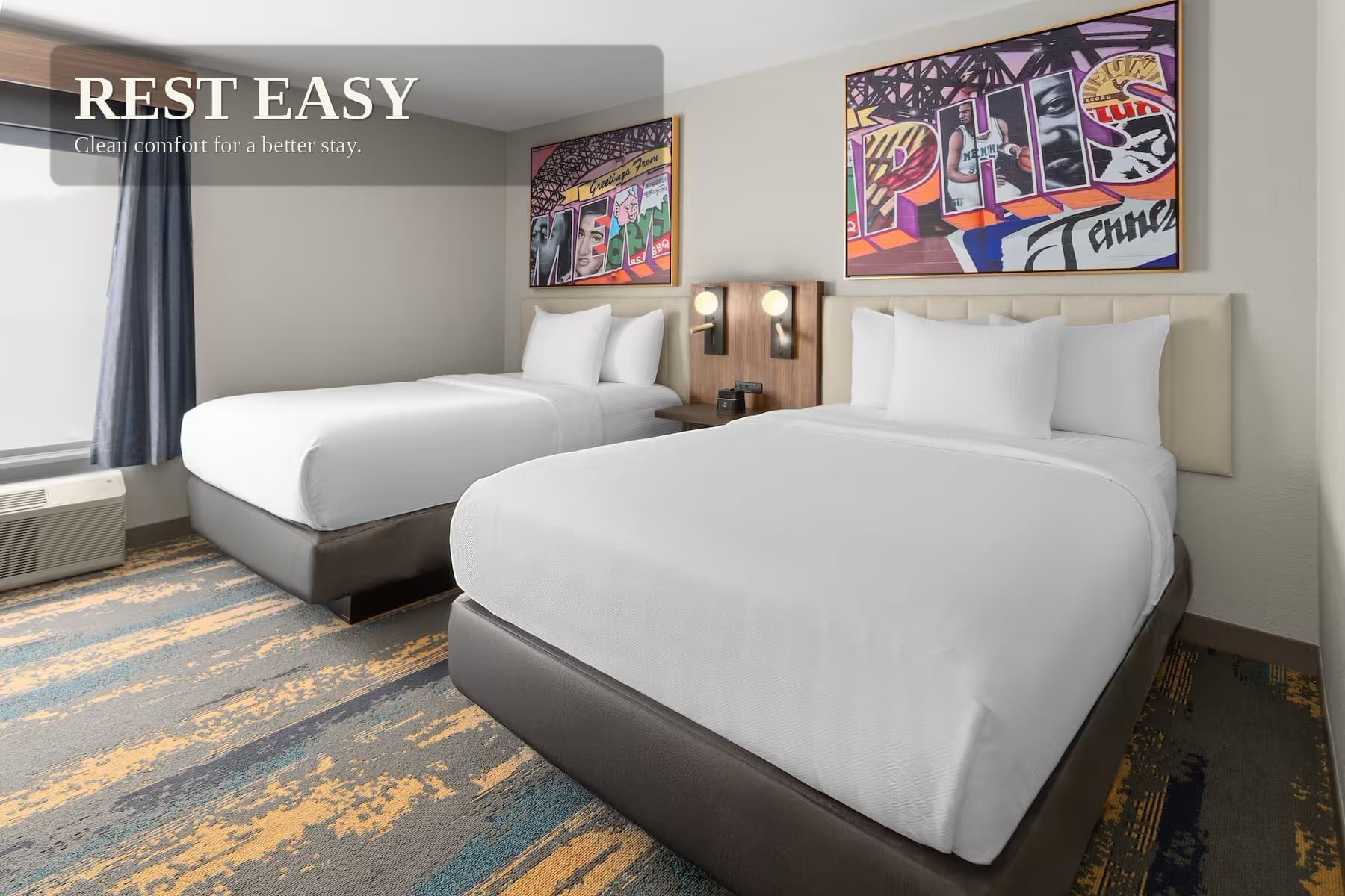 A guest room with two queen beds, wall-mounted reading lights between them and framed Memphis artwork above the headboards.